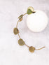 Decorative wreath with green leaves around a white ceramic vase on a light gray background