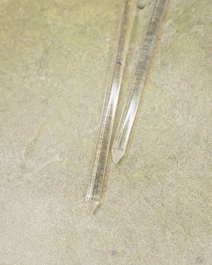 Two clear crystal sticks on a textured beige surface